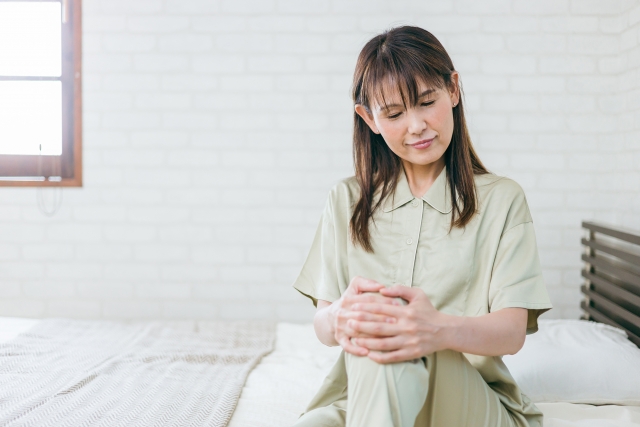 ベッドに座って膝に手を置く女性