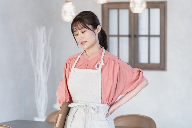 エプロン姿の女性が腰に手を当てて疲れた表情をしている